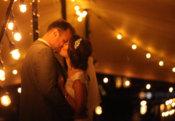 Wedding Bride and Groom kiss below festoon lights