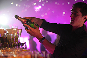 Image of a waiter pouring a drink from a bottle into glasses at an event